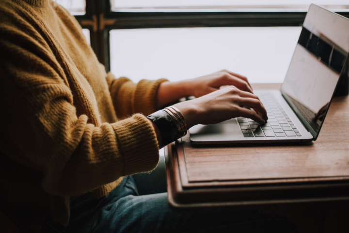 Picture shows an individual sitting in front of a laptop typing