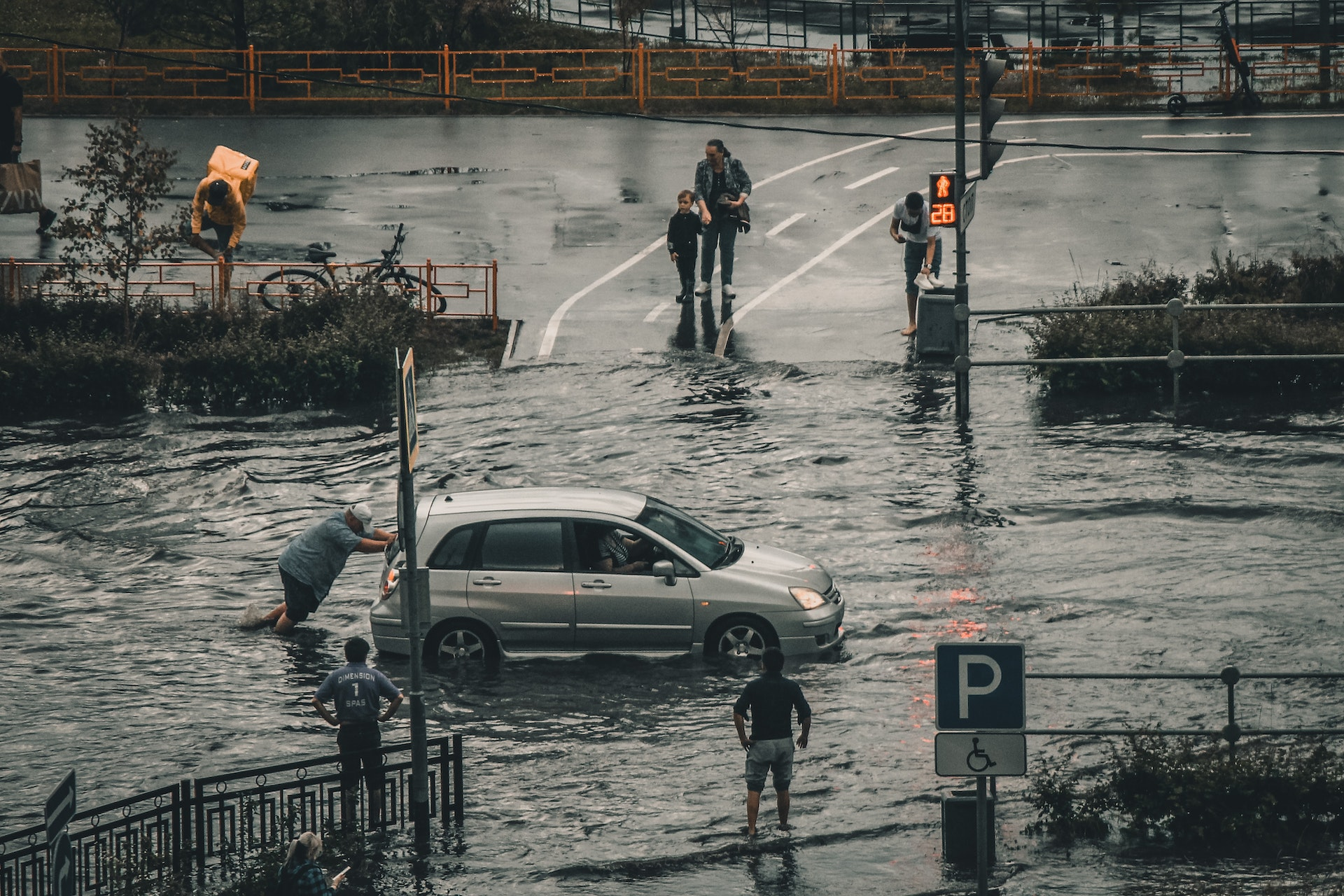 Flooding in a busy intersection with cars and pedestrians. Workers helping with disaster response.